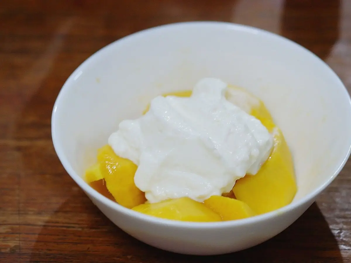 Cuenco blanco con yogur y trozos de mango amarillo sobre una mesa de madera