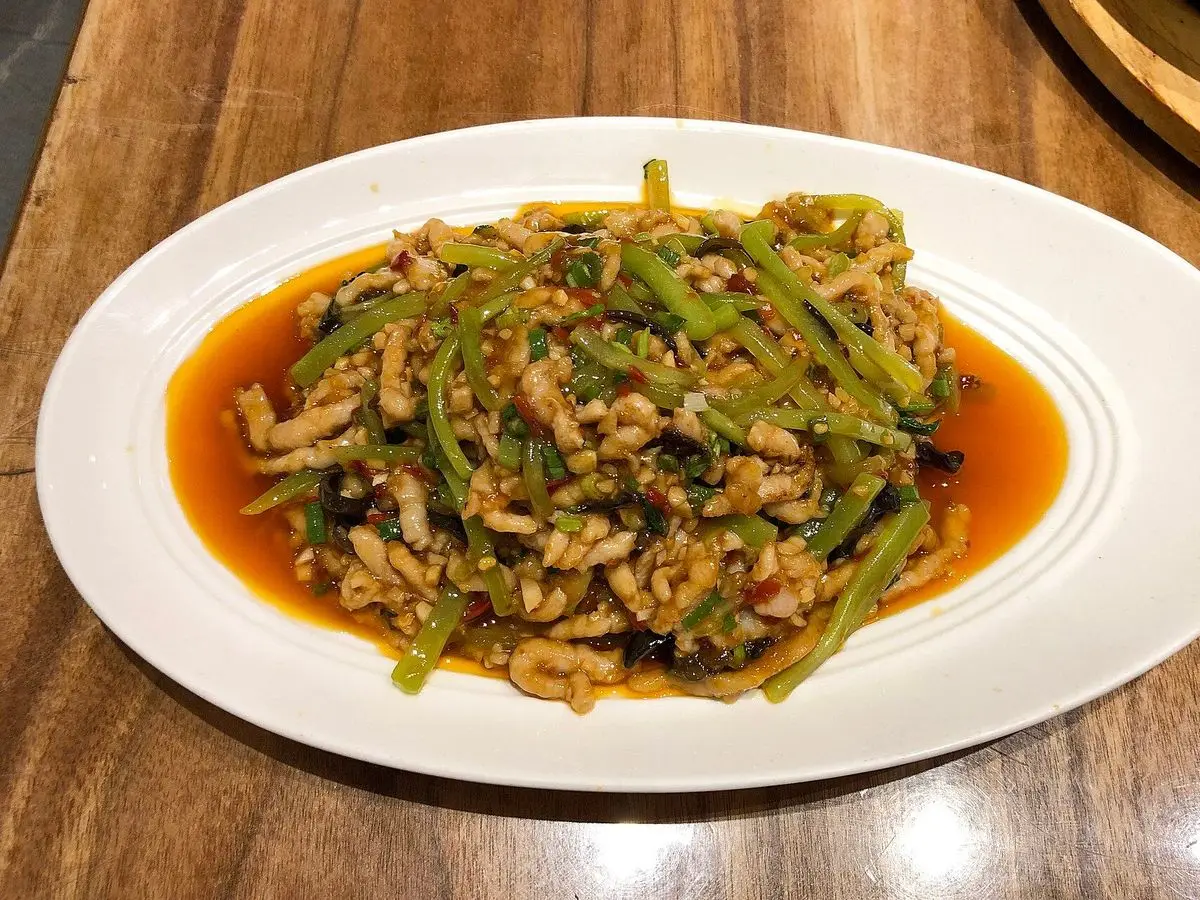 Plato blanco de tiras de cerdo salteadas con pimiento verde en salsa rojiza