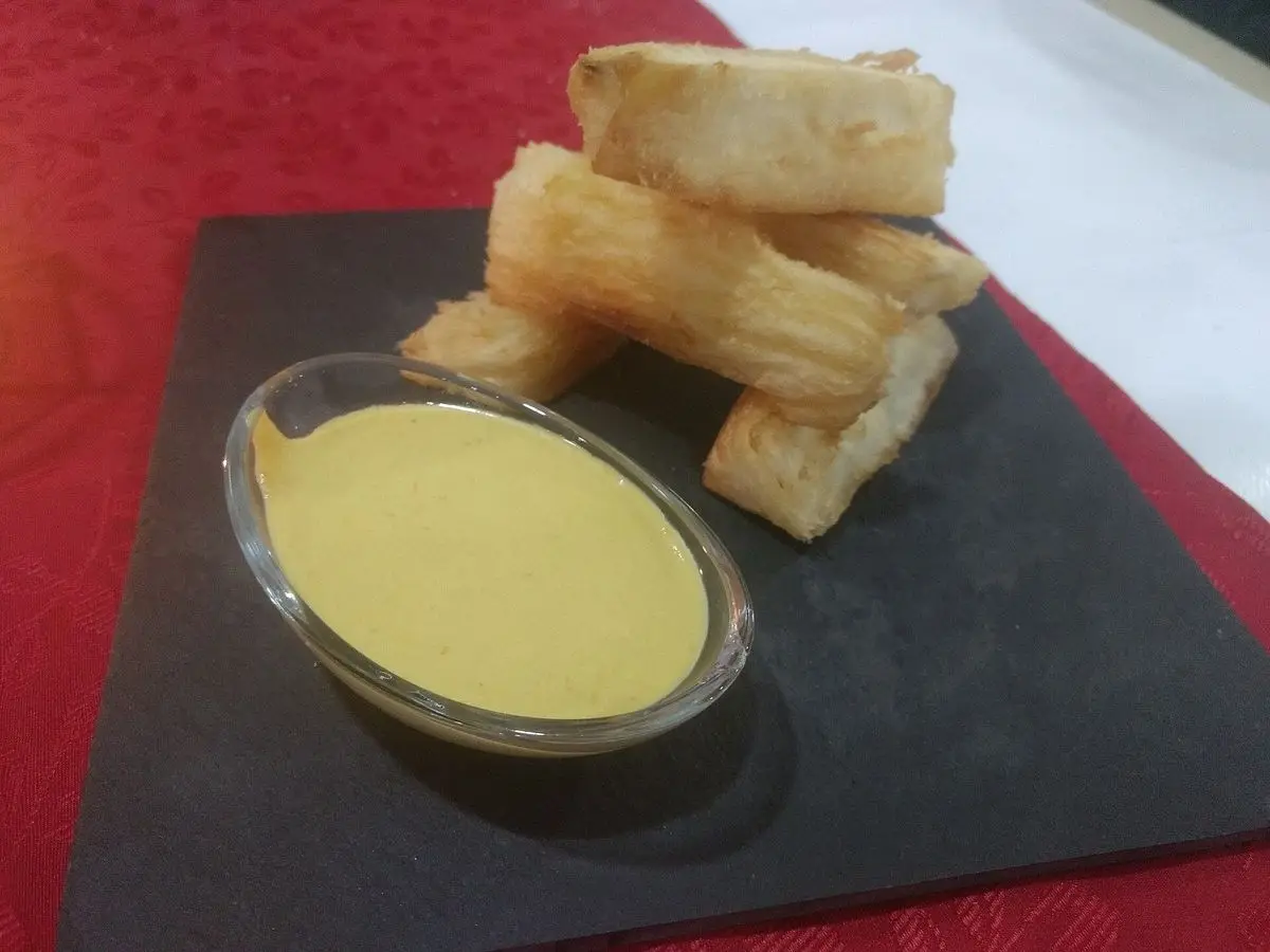 Bastones de yuca dorada y crujiente con un cuenco de salsa cremosa amarillenta sobre pizarra negra
