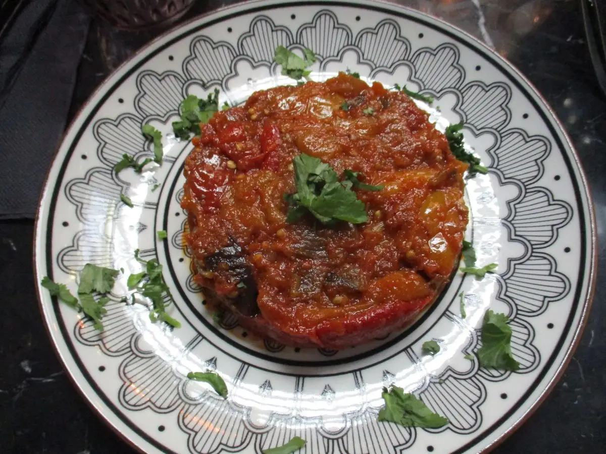 Plato con puré de berenjena y tomate especiado, decorado con una hoja de perejil