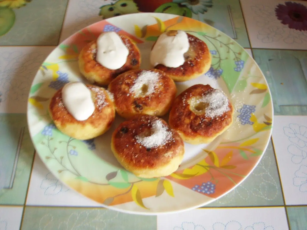 Tortitas de requesón doradas con una cucharada de nata agria sobre un plato de flores