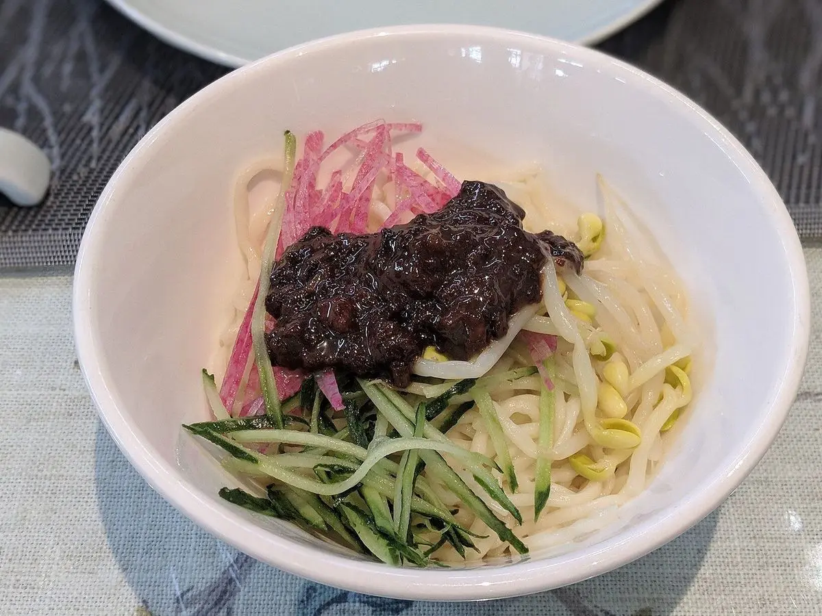 Cuenco blanco de fideos con salsa oscura de soja y carne, pepino en tiras y rábano