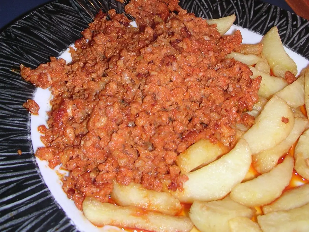 Plato de picadillo de chorizo desmenuzado junto a un cuenco de patatas cocidas en la mesa