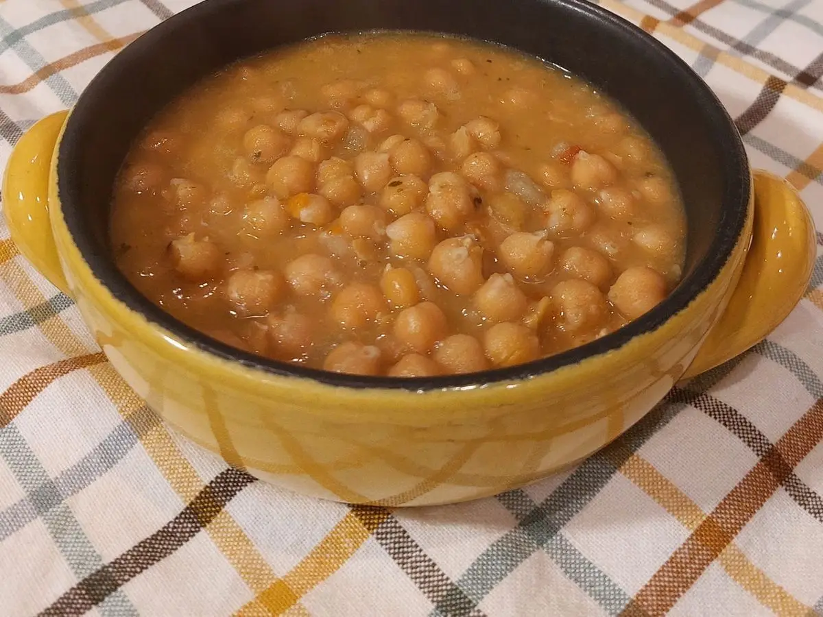 Cuenco amarillo de sopa espesa de garbanzos sobre un mantel de cuadros